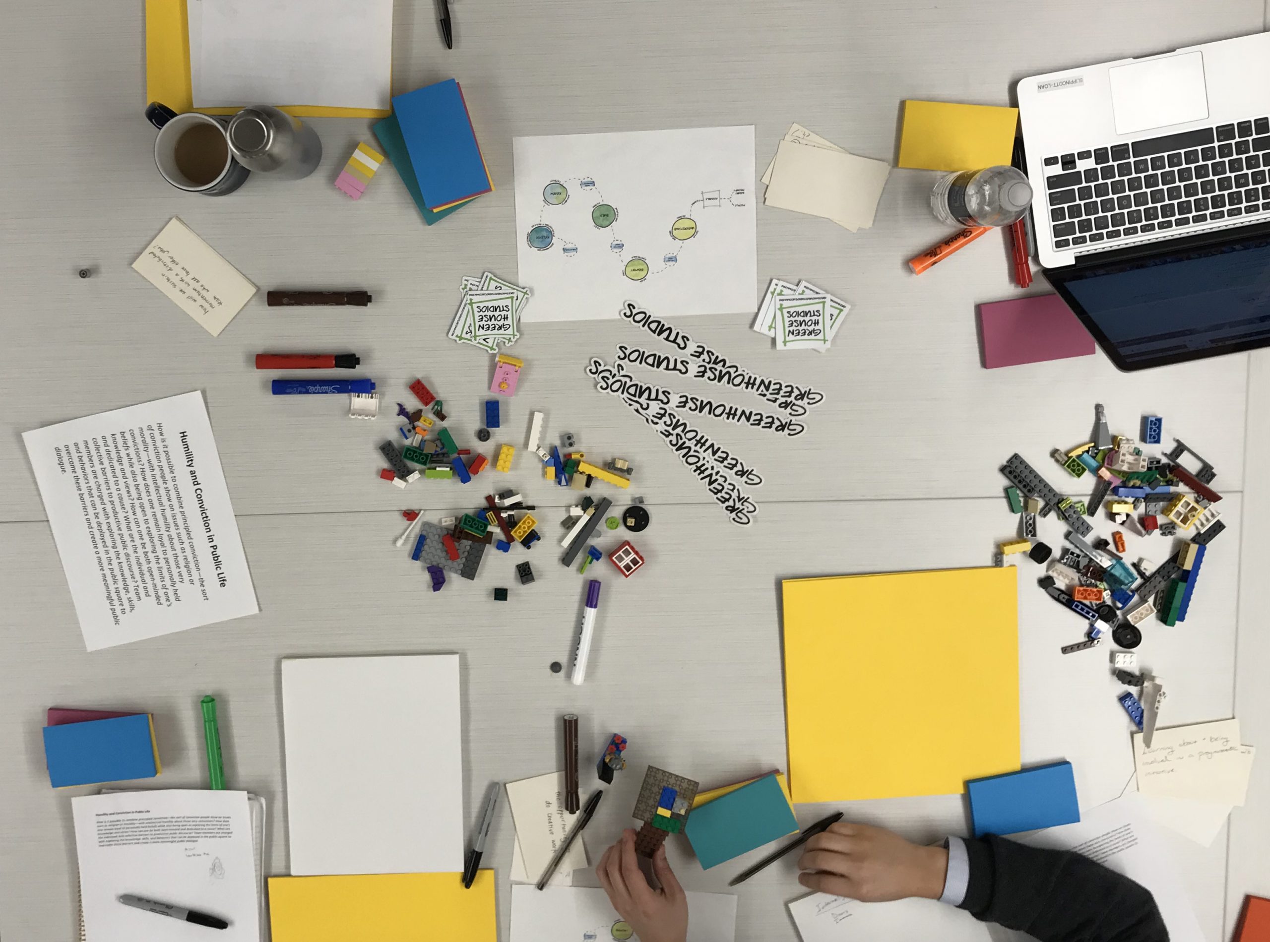 table being used for brainstorming with pens, paper, legos, and other items scattered about.